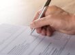 Hand holding pen, filling out a tick-box form or survey on a sheet of paper on a desk.