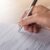 Hand holding pen, filling out a tick-box form or survey on a sheet of paper on a desk.