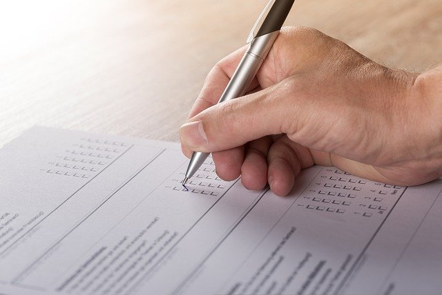 Hand holding pen, filling out a tick-box form or survey on a sheet of paper on a desk.