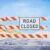 A Road Closed sign blocks a deserted road with sand dunes and blue sky in the background.